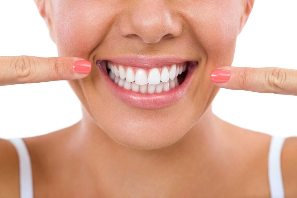 Woman pointing at her smile, illustrating the question of whether the dentist is responsible for a failed crown